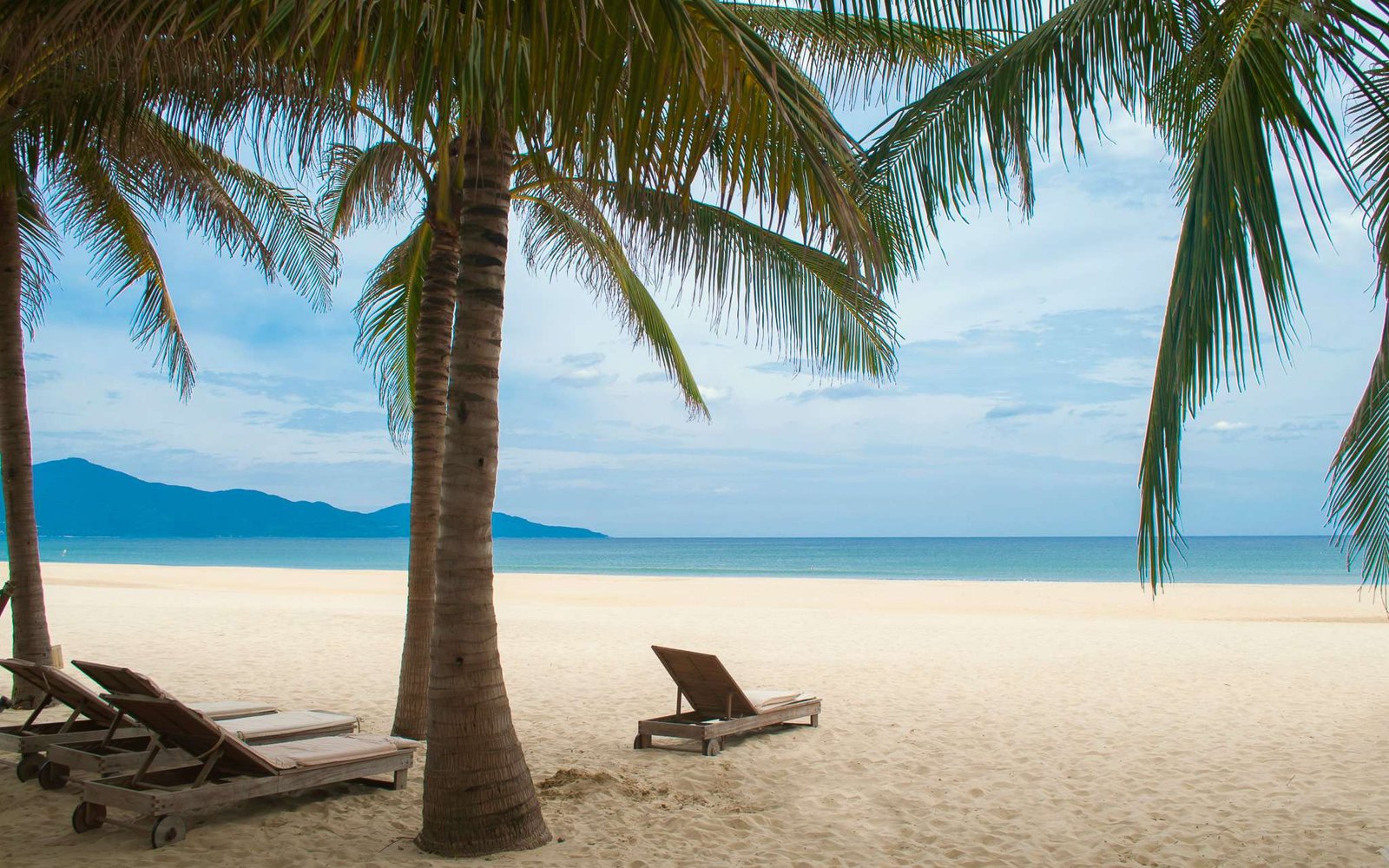 Espreguiçadeiras, areia, mar azul e palmeiras na praia de My Khe.