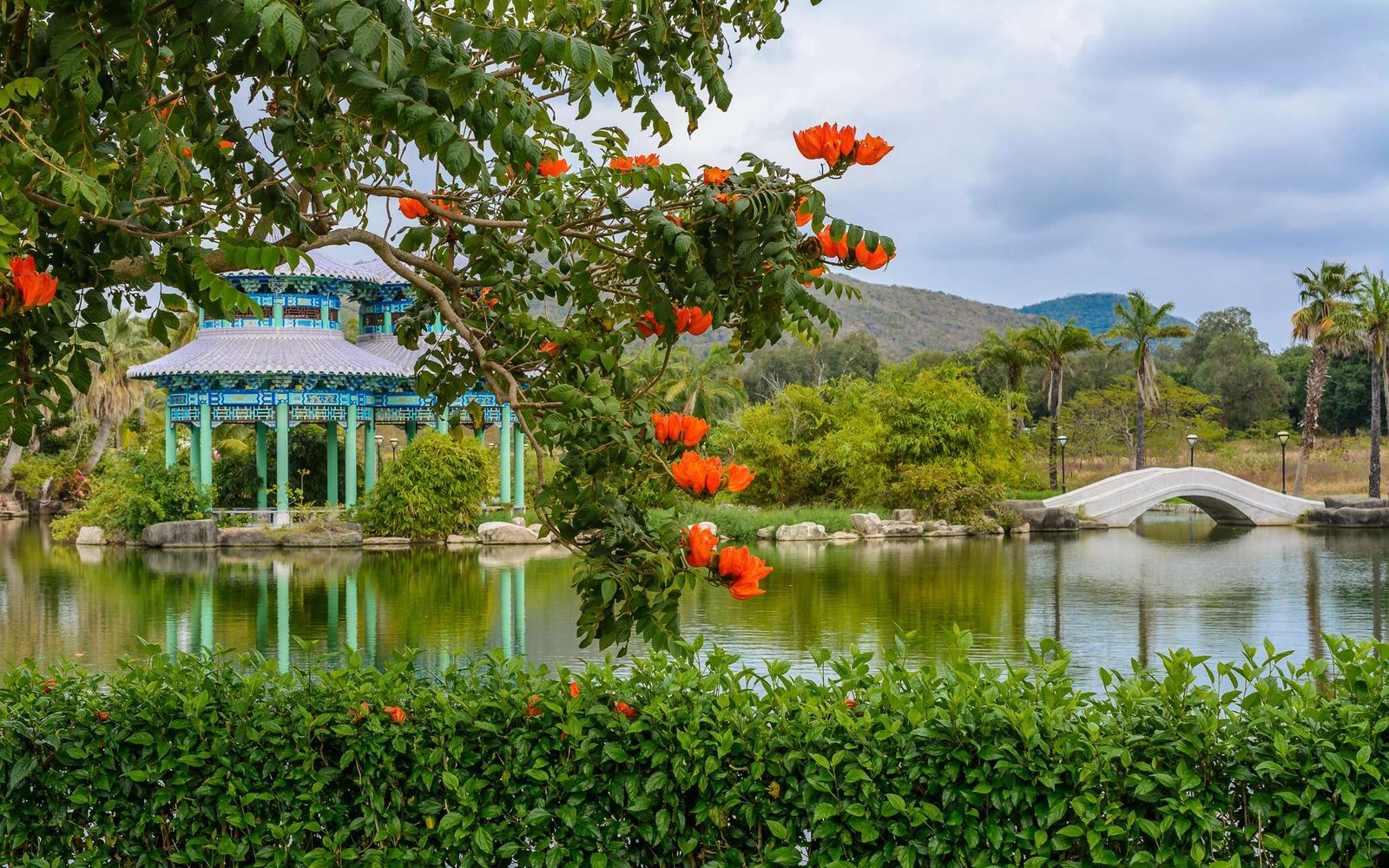 Green lake surrounded by gazebos, temples, mountains, fowers, palm grove and stone fence on the territory of Buddhist center Nanshan, in Sanya, Hainan, China.