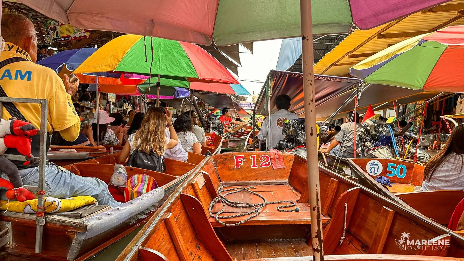 Crowd of tourists under colorful umbrellas at a boat gridlock at the floating market