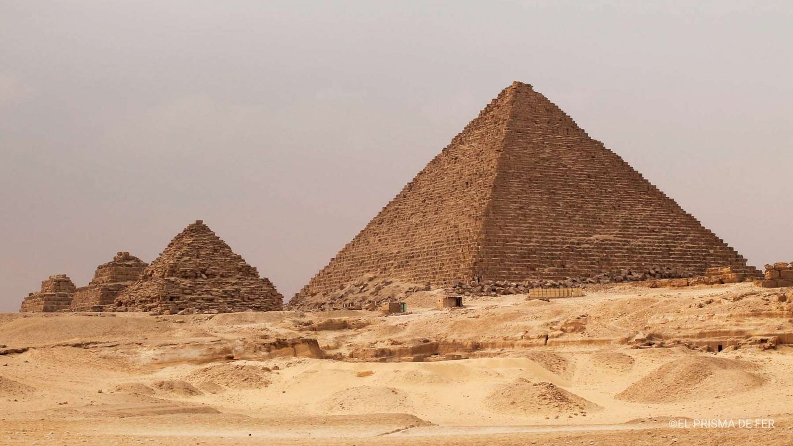 As Pirâmides de Gizé vistas do deserto, com destaque para a Pirâmide de Khafre e as pirâmides menores ao redor, banhadas pela areia dourada e pela luz quente do sol do Egito.