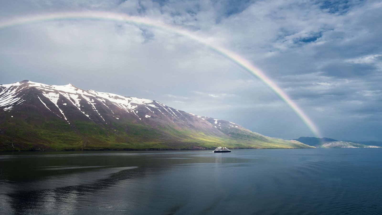 Arco-íris perto de Akureyri, Islândia, rodeado por paisagens montanhosas e natureza selvagem.