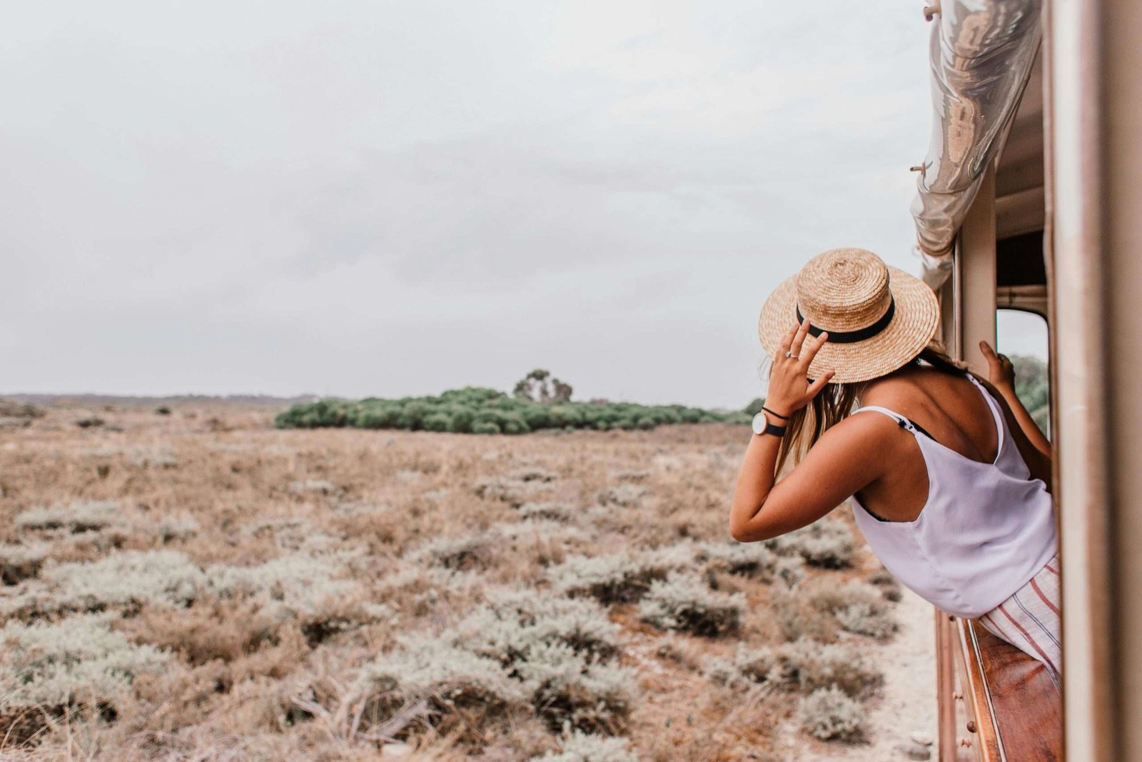 Woman with straw hat looking out train window at scenic countryside. Adventure awaits.