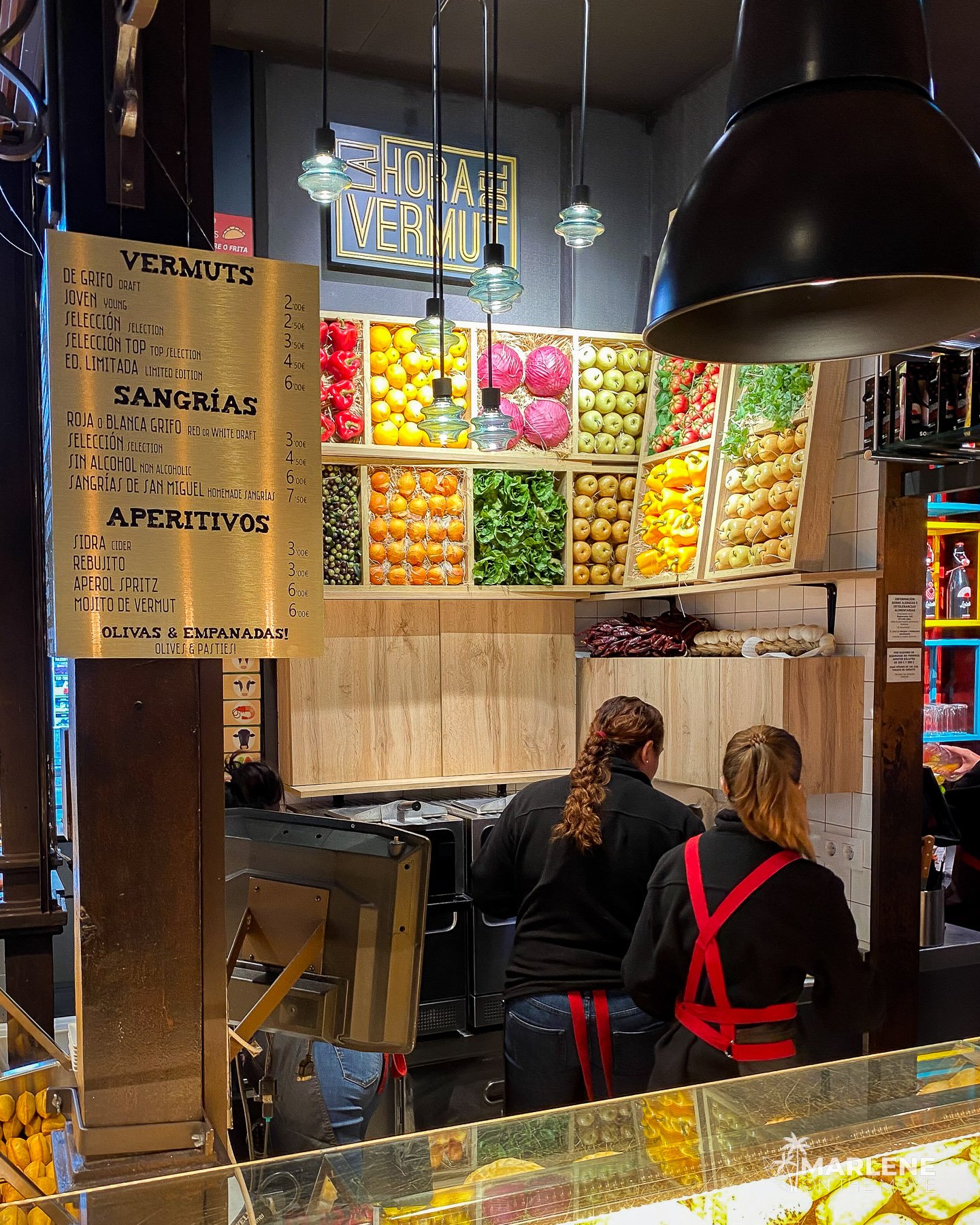 Food and drink stall inside Mercado de San Miguel, decorated with fruit and vegetables.