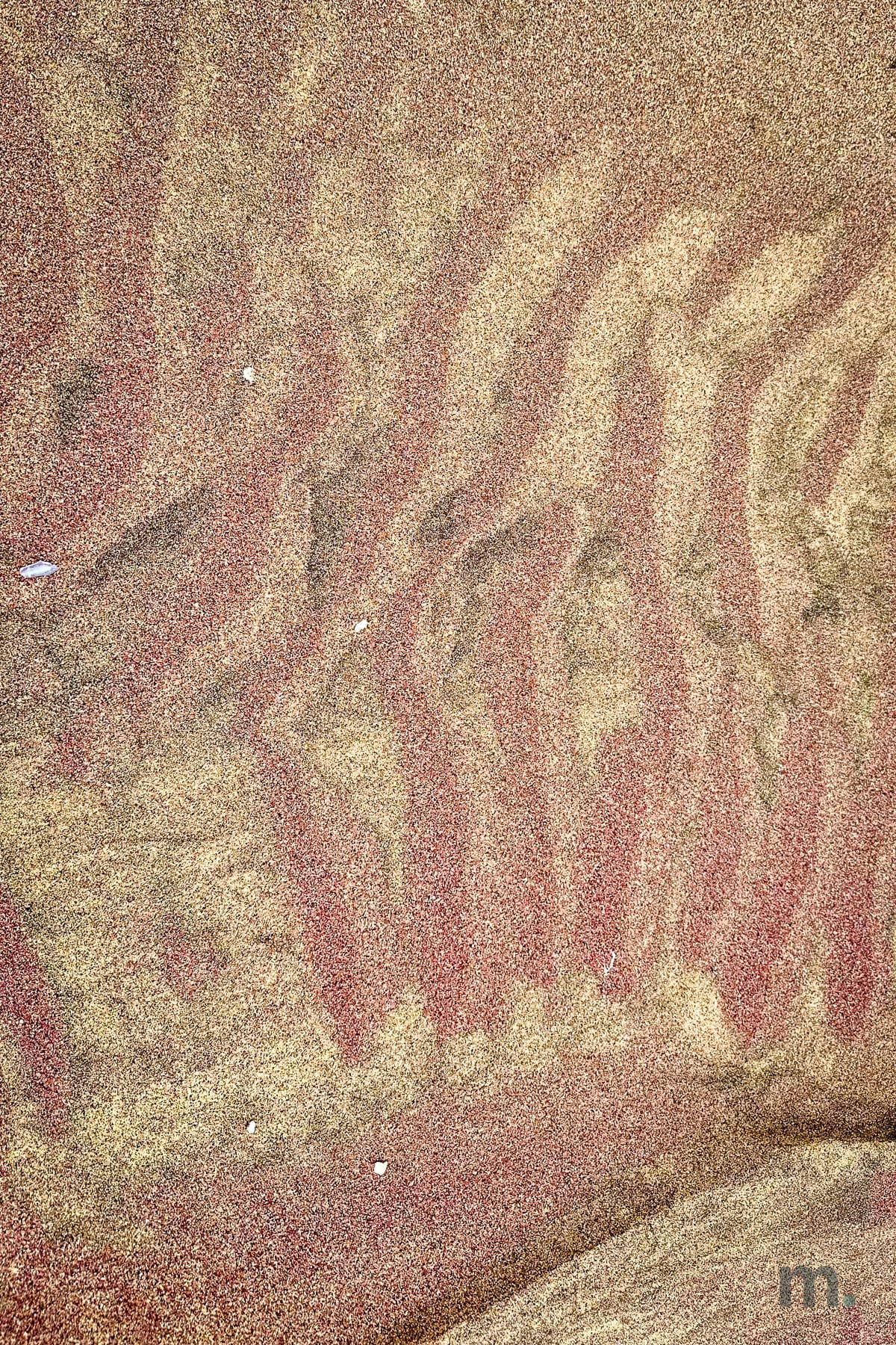 Pink and ochre sand patterns left by the tide on the beach at Sandwich Harbour
