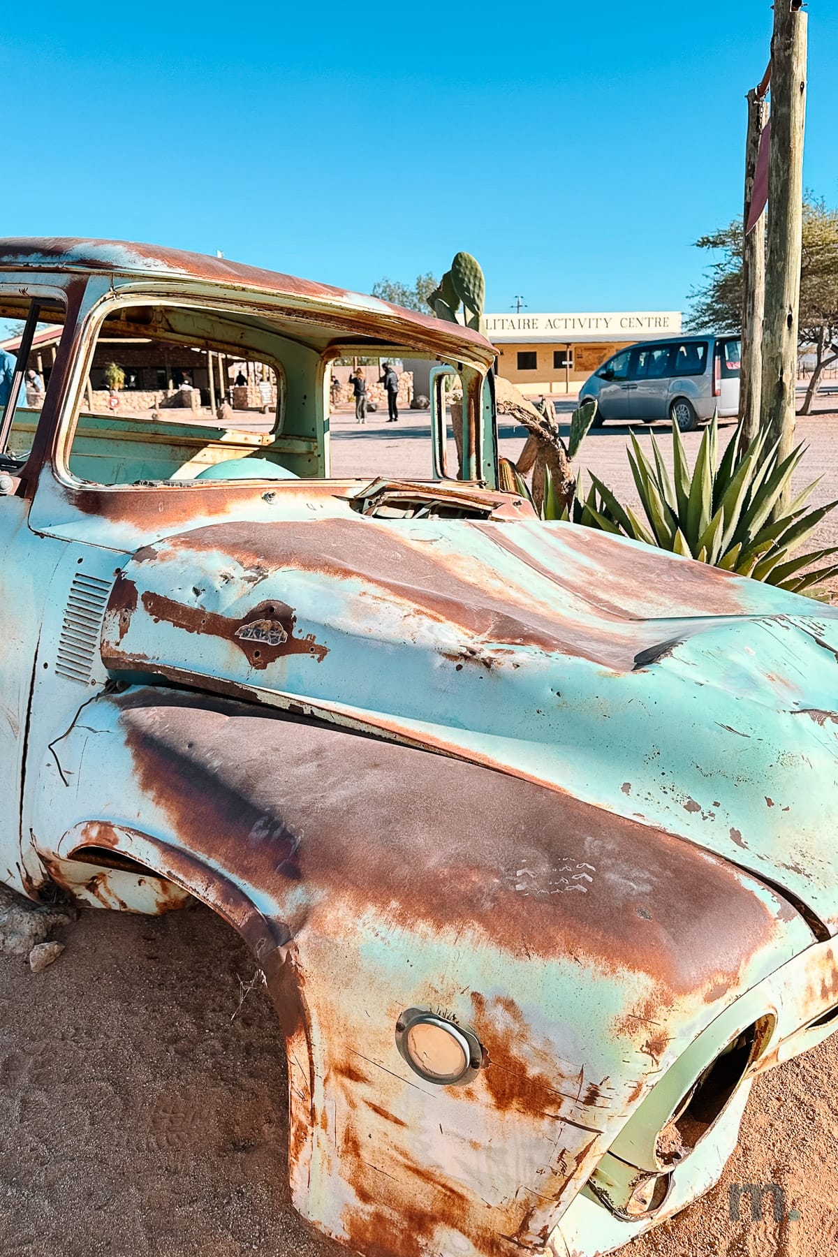 Rusted vintage car abandoned at Solitaire, activity centre behind