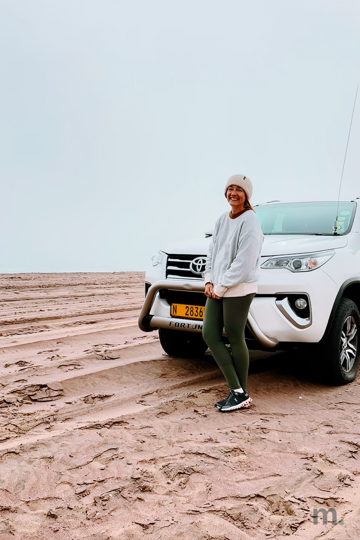 Marlene beside the 4WD on the wet sand at Sandwich Harbour in coastal fog